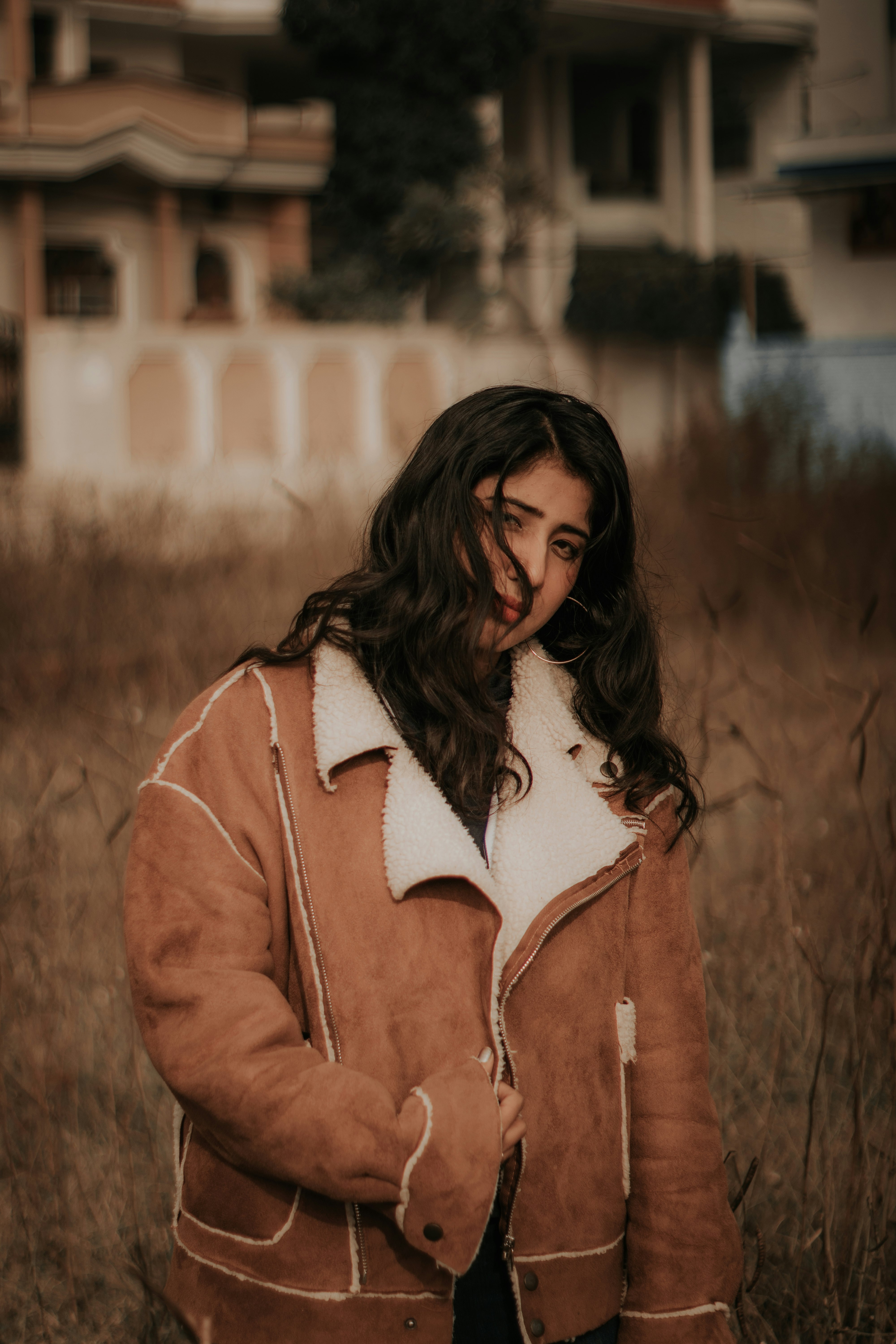 woman in brown jacket standing on brown grass field during daytime